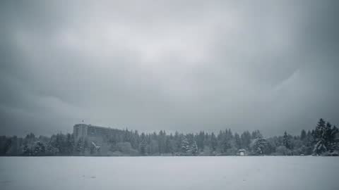 Snow Drifting Over Suburban Field with Apartment Building Left and Gazebo Right Under Overcast Sky