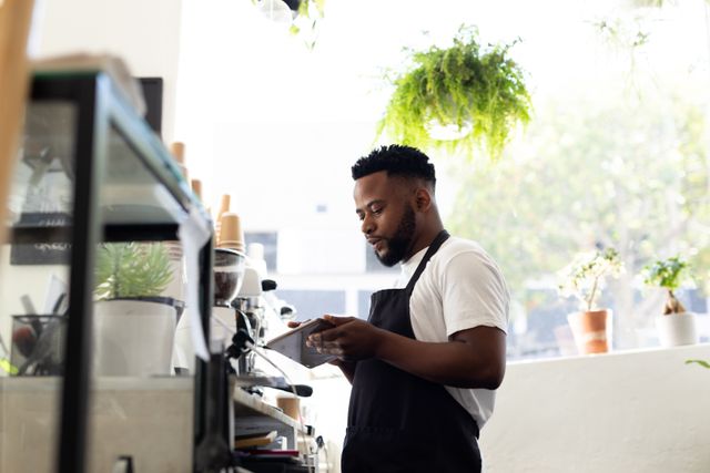 Young male african american barista using tablet pc in kitchen at cafe. unaltered, cafe culture, people, occupation and technology concept.