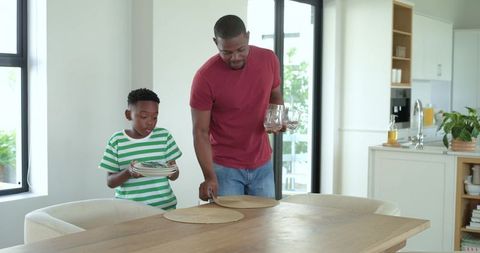 African American Father and Son Preparing Dining Table Together in Bright Modern Kitchen