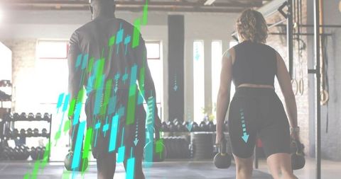 Partners carrying kettlebells in warehouse gym walking through open-plan workout space