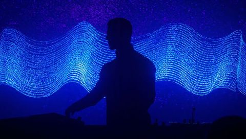 Silhouette dj mixing amid neon blue led waveform backdrop for futuristic club performance