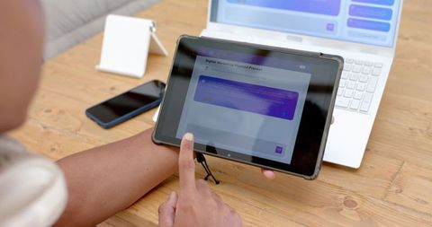 Holding Tablet Tapping Touchscreen on Wood Desk for Remote Digital Marketing Planning