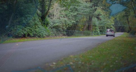Silver minivan driving through tree-lined road with faint map overlay and autumn foliage