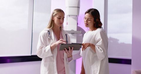 Female radiologist reviewing mammogram results with patient pointing at tablet in clinic