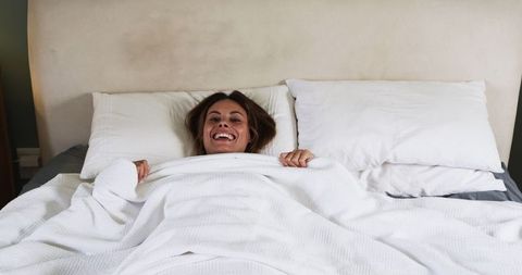Smiling Woman Relaxing with Cozy Duvet in Tranquil Bedroom