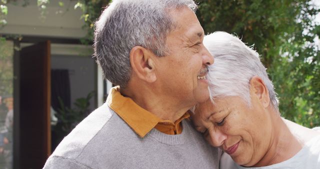 Elderly couple sharing an affectionate hug outdoors under trees, both smiling and enjoying each other's company. Ideal for illustrating themes of love, companionship, and happiness in senior years. Perfect for use in retirement planning advertisements, health care services, lifestyle blogs, or family-oriented content.