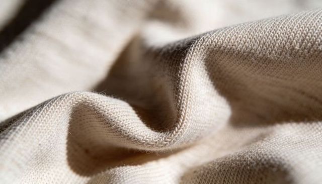 Beige knit fabric macro texture showing soft folds, stitch detail and natural fibers
