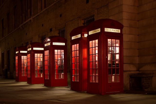 Classic British red telephone boxes illuminated at night, creating a nostalgic scene on a dimly lit street in London. This image can be used for websites, travel brochures, or promotional materials highlighting iconic British culture, historical themes, or nighttime cityscapes.