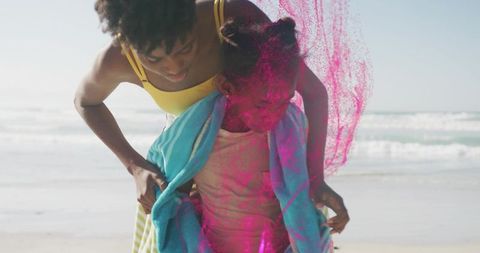 Wrapping child in towel on sunny beach with vibrant pink powder splash