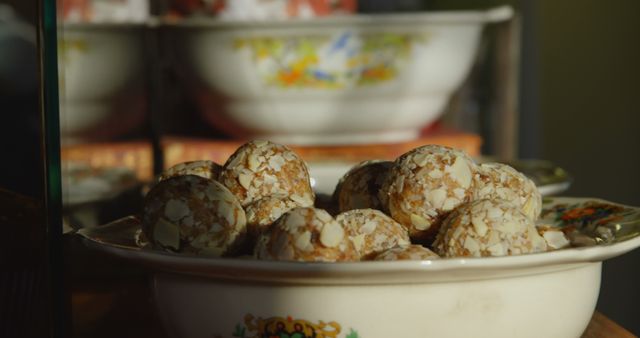 The image shows almond energy balls arranged in an ornate, vintage dish with colorful floral patterns. This setup creates a nostalgic and inviting look, perfect for highlighting healthy eating or traditional home cooking. Could be used in advertisements for nutrition and wellness products, recipe blogs, or lifestyle magazines focusing on homemade, traditional foods. Ideal for promoting healthy desserts or as a feature image for diet and nutrition articles.