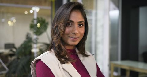 Confident indian businesswoman posing in modern office wearing burgundy top and beige vest