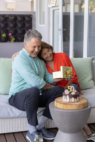 Mature couple celebrating 50th anniversary on patio exchanging gift and sharing laughter