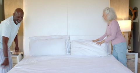 Senior Couple Arranging Bed Together in Comfortable Bedroom