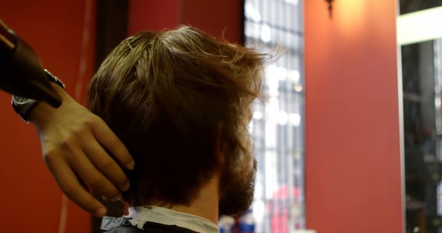 A man is getting his hair styled by a professional barber in a salon setting. The barber is using a hair dryer to style the man's hair. Ideal for use in articles or advertisements related to men's grooming, professional barber services, hair care tips, salon marketing, or fashion and style.