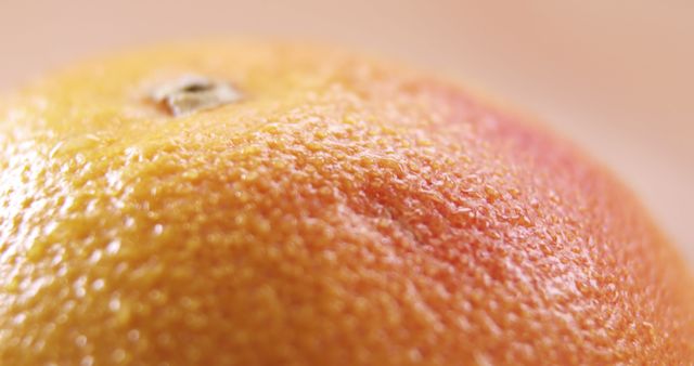 Close-up of an orange's textured surface, highlighting the pores and vibrant color of the fruit's skin. Its detailed texture and color saturation suggest freshness and natural ripeness.