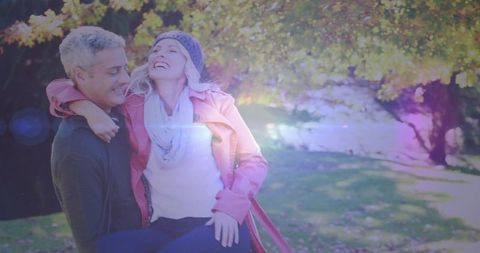 Mature couple embracing and laughing by autumn waterside with warm lens flare