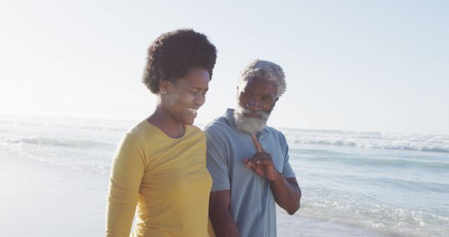 Happy african american couple walking and talking on sunny beach. healthy and active time beach holiday.