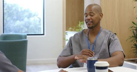African american male nurse relaxing in staff lounge discussing with coworker over coffee
