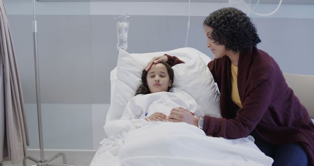 Mother is sitting beside her daughter who is lying in a hospital bed with an IV drip. She is gently touching her daughter's forehead, showing care and concern. This image can be used to depict themes such as caregiving, family support during illness, parent-child relationship, medical treatment, and recovery in healthcare and wellness contexts.
