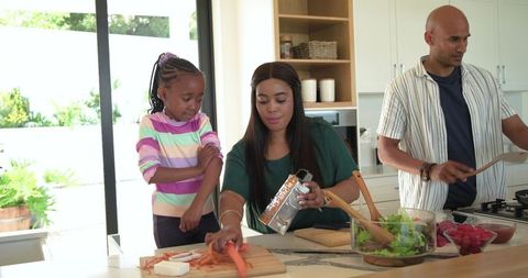 Family preparing healthy dinner together on kitchen island chopping carrots and tossing salad
