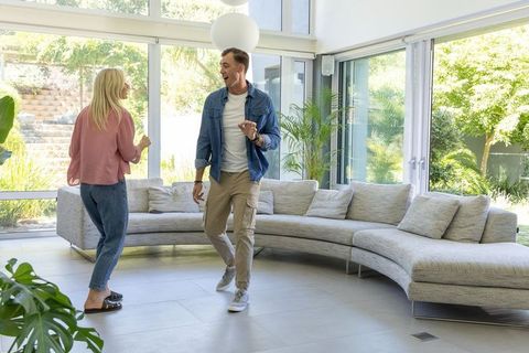 Couple dancing in bright modern living room with curved sofa and floor-to-ceiling windows