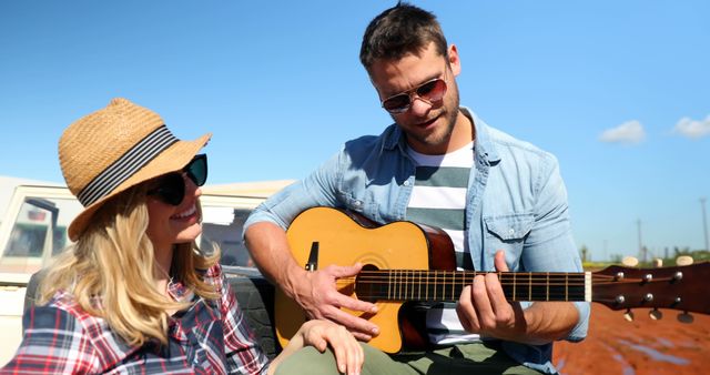 Caucasian couple enjoys music outdoors, with copy space. He plays the guitar for her, adding a romantic touch to their road trip.