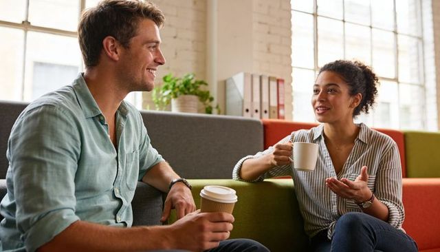 Colleagues sharing coffee during casual office lounge conversation in modern workspace