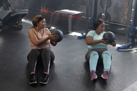 African american women partner training with medicine balls working core strength in gym
