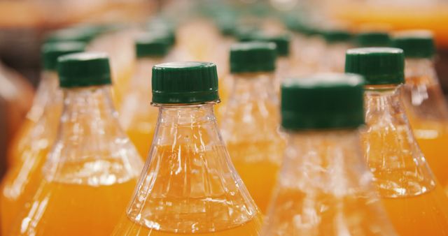 Lines of orange juice bottles with green caps on an assembly line in a factory setting. This image can be used to illustrate concepts related to beverage production, manufacturing processes, healthy drinks, freshness, and market products. It is suitable for websites and materials of food and beverage companies, logistics, supply chain, and industrial manufacturing articles.