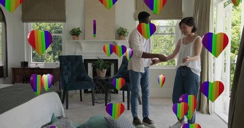 Couple holding hands in sunlit bedroom with rainbow hearts celebrating lgbtq love