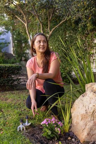 Woman Gardening Pink Flowers with Trowel in Scenic Backyard