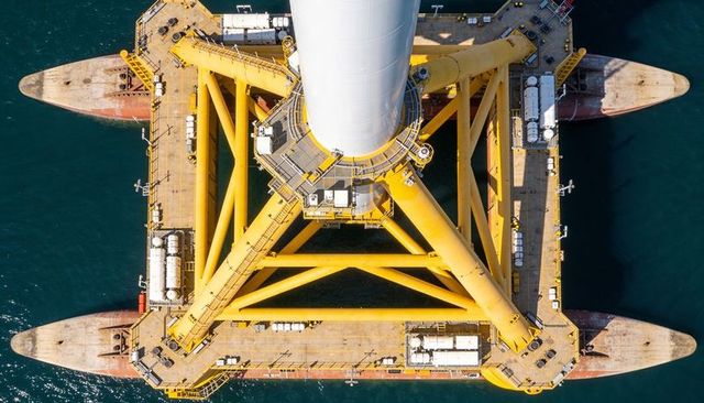 Aerial top view of yellow jacket foundation on barge transporting wind turbine tower
