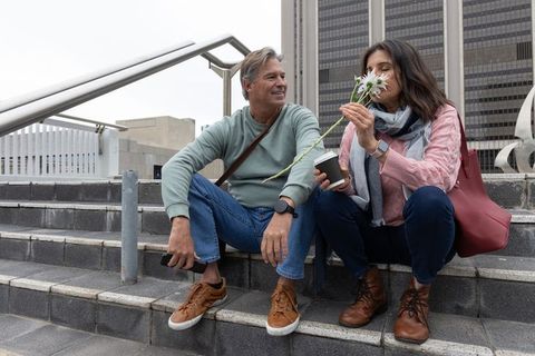 Senior couple sharing quiet moment on city steps smelling flowers and sipping coffee