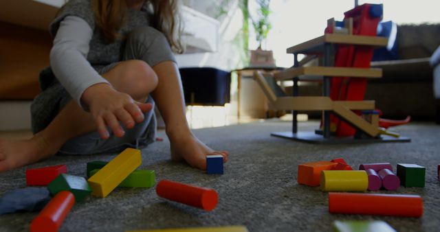 Young child having fun building and exploring with colorful wooden blocks on the floor. Ideal for themes related to childhood development, educational toys, creative play, family activities, and children's learning environments.