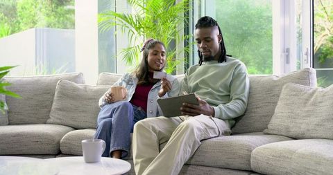 Couple shopping online on tablet while holding credit card on cozy modern living room sofa