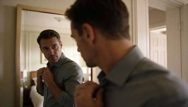 Man adjusting collar in mirror during morning routine preparing for work, thoughtful