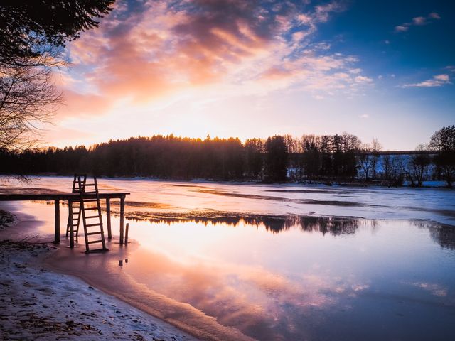 Evoking a sense of peacefulness and calm, this scenic view of a sunset over a frozen lake with a wooden pier and staircase makes it perfect for use in themed websites, blogs, nature calendars, postcards, seasonal greeting cards, and serene landscape-focused marketing materials.