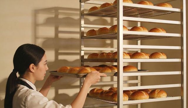 Baker placing fresh golden rolls on commercial stainless rack in professional bakery