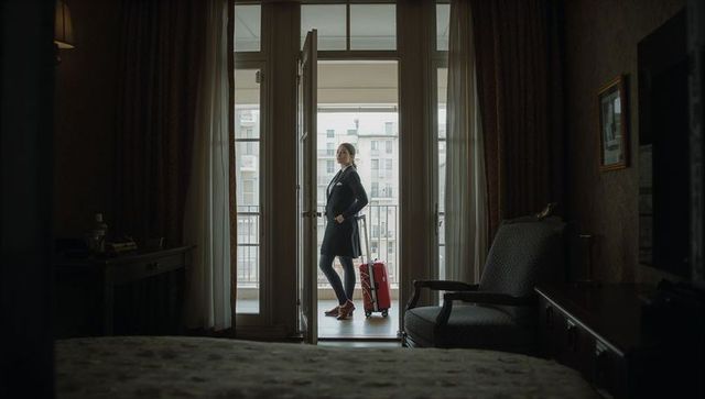 Business traveler standing at balcony door with red suitcase in boutique hotel room