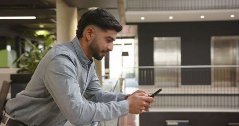 Man Engaged with Smartphone in Modern Office Atrium
