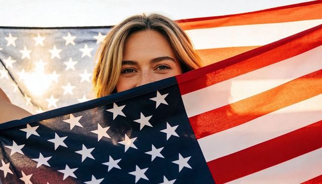 Young woman holding american flag, sunlit patriotic portrait, smiling eyes peeking