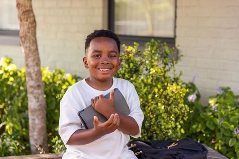 Smiling african american boy holding tablet on bench back-to-school outdoor learning