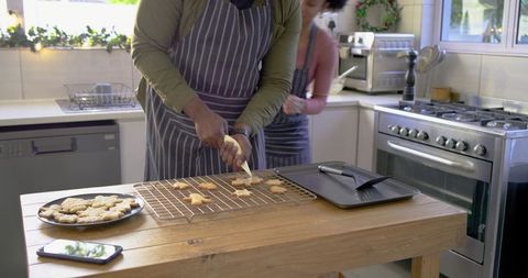 Diverse couple decorating star cookies on island wearing striped aprons holiday baking