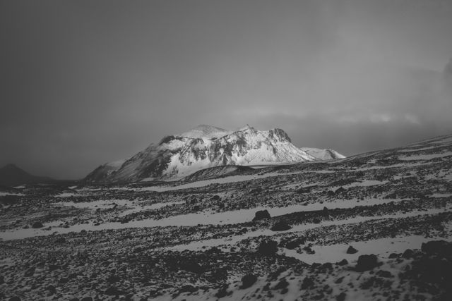 Snow-covered mountain standing majestically in a desolate winter landscape. Sky appears overcast, emphasizing the isolation and serenity of the location. Ideal for use in nature-themed projects, travel blogs focusing on remote destinations, or artistic expressions of solitude and natural beauty.