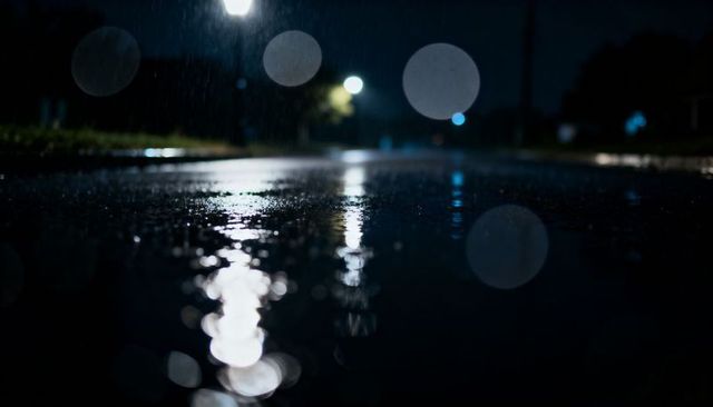 Moody rainy night road with wet pavement reflections and streetlight bokeh cinematic background