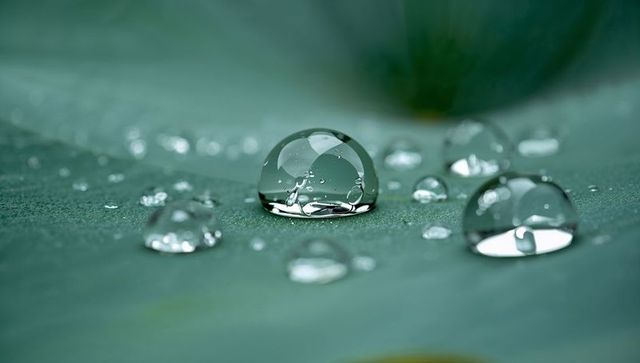 Glistening macro water droplet on green leaf with crystal dew beads and soft bokeh