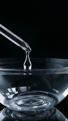 Vertical macro video of glass dropper releasing water droplet into glass bowl creating ripples