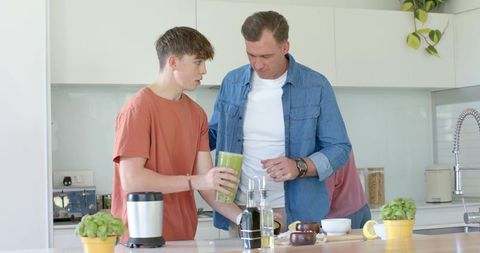 Father helping teen preparing green smoothie in bright modern kitchen