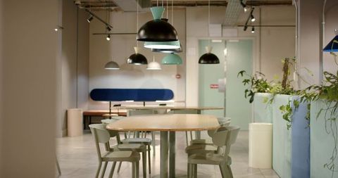 Minimalist coworking lounge with communal wooden table, molded chairs, pendant lights