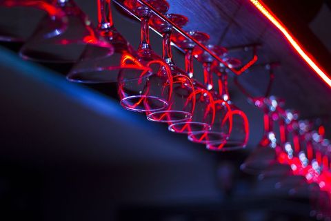 Hanging wine glasses reflecting red neon light, stylish bar interior mood